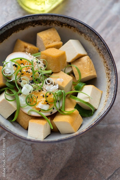 Fototapeta Bowl with smoked tofu cheese, soy-marinated egg and spring onion, vertical shot on a brown granite background, middle closeup