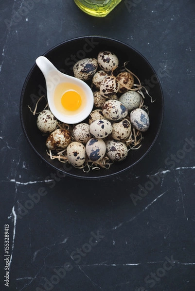 Fototapeta Bowl with raw fresh quail eggs on a black marble background, vertical shot, copy space, top view