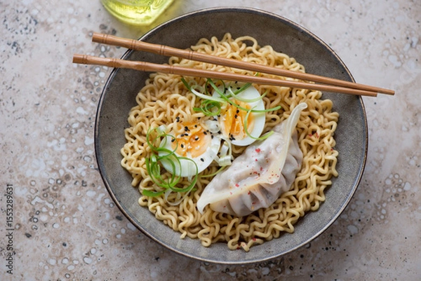 Fototapeta Plate of ramen noodles with boiled egg and steamed dumpling on a beige granite background, horizontal shot, elevated view