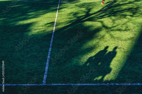 Fototapeta A soccer field with a shadow of two people on the grass. The shadow is on the grass and the people are not visible