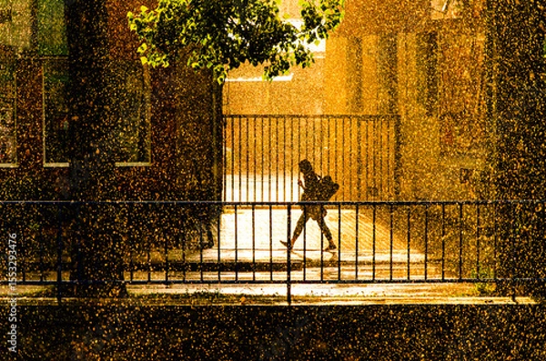 Fototapeta A person is walking on a sidewalk in the rain. The person is wearing a backpack