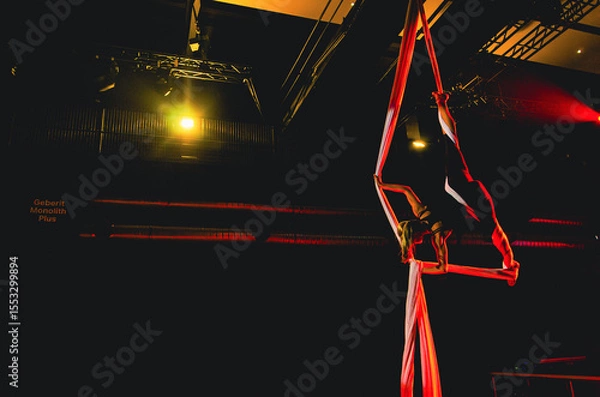 Fototapeta A person is performing a trick on a tightrope. The tightrope is red and the person is wearing black