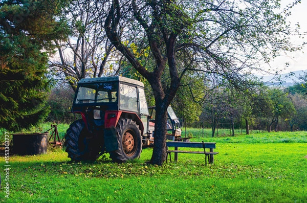 Fototapeta A tractor is parked in a field next to a tree. There is a bench in the field