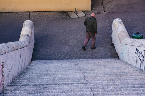 Fototapeta A man walks down a set of stairs. The stairs are made of concrete and are covered in graffiti