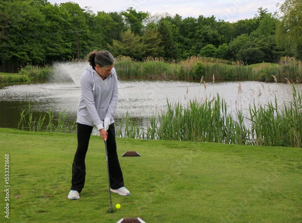 Obraz Woman Practicing Golf Swing on a Course by a Lake