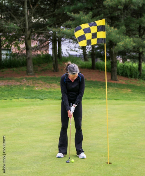 Obraz Woman Preparing to Putt on a Golf Course Surrounded by Trees