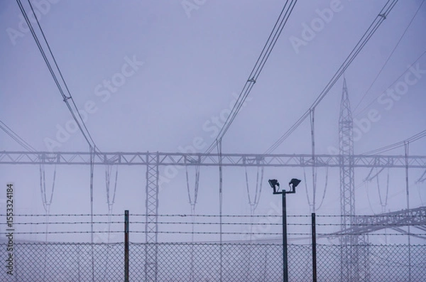 Fototapeta A fence with wires and poles in the background. A man is standing in front of the fence