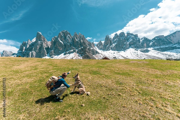 Fototapeta Hiker with dog enjoying scenic view of snowy mountain peaks in the Dolomites, Italy.