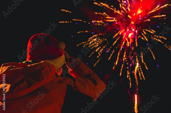 Fototapeta A person in a red hat is watching fireworks in Christmas time. Santa cap