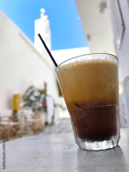 Fototapeta Closeup view of a Greek freddo espresso with rich crema, set against a softly blurred background of a picturesque Cycladic island, evoking summer vibes, relaxation, and Mediterranean charm.