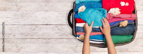 Obraz Kobieta pakująca bagaż na nową podróż na drewnianej podłodze. Miejsce na Twój tekst.