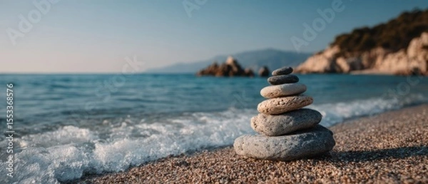 Fototapeta Balanced pebble tower on a sunlit beach with ocean wave and peaceful summer mood, banner