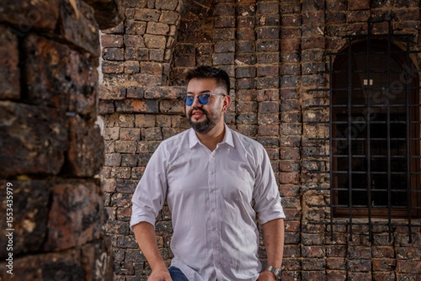 Obraz Bearded Latino man posing with attitude in a colonial castle structure in daylight. Fashion, modeling, tourism, and style concepts.