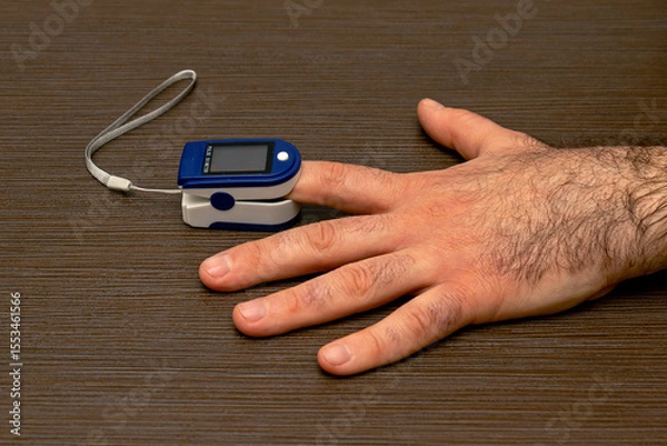 Obraz Male hand holding pulse oximeter on index finger measuring level of oxygen in blood