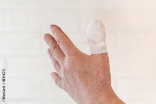 Fototapeta Bandaged left thumb against a light wall. Cuts, Injuries and First Aid