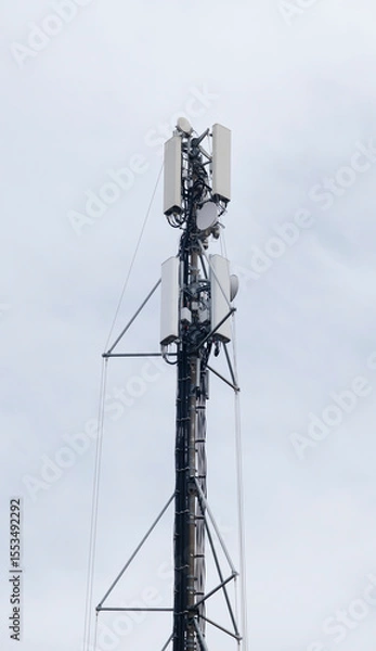 Obraz Tall cellular communication tower with multiple antennas and equipment mounted on metal framework against overcast sky. Telecommunications infrastructure for mobile networks and data transmission.

