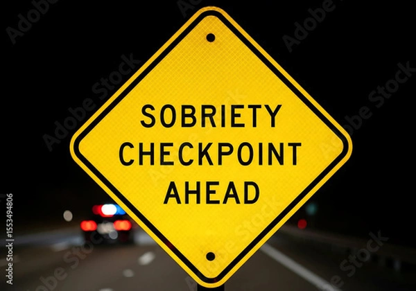 Fototapeta Sobriety Checkpoint Warning Sign at Night with Reflective Surface and Blurred Car Lights in Background