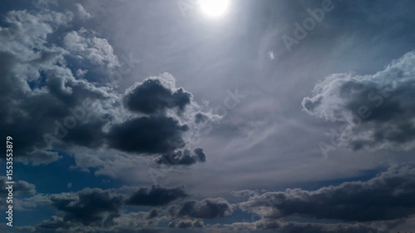 Obraz Dramatic sky with dark clouds and a bright sun illuminating the scene, creating a striking contrast. Perfect for backgrounds, weather themes, or artistic projects.