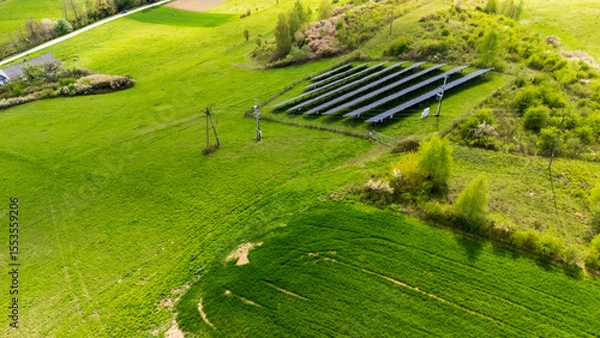 Obraz Aerial view of a solar panel installation on a lush green field, emphasizing renewable energy use in rural areas, surrounded by nature and agricultural land.