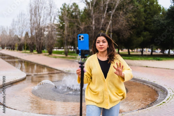 Fototapeta Influencer creating content in urban park using smartphone and tripod