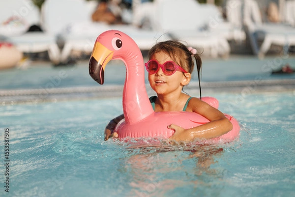 Fototapeta Cute funny toddler girl in a sunglasses relaxing on inflatable toy ring floating in pool have fun during summer vacation. Child having fun in swimming pool. 