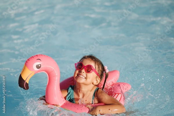 Fototapeta Cute funny toddler girl in a sunglasses relaxing on inflatable toy ring floating in pool have fun during summer vacation. Child having fun in swimming pool. 