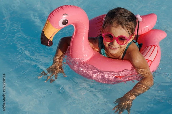 Fototapeta Cute funny toddler girl in a sunglasses relaxing on inflatable toy ring floating in pool have fun during summer vacation. Child having fun in swimming pool. 