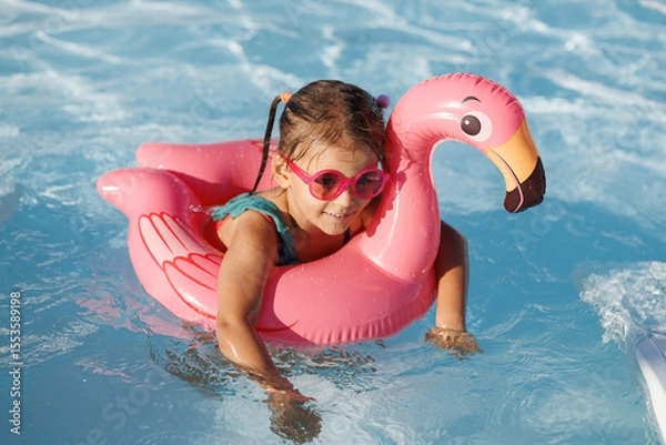 Fototapeta Cute funny toddler girl in a sunglasses relaxing on inflatable toy ring floating in pool have fun during summer vacation. Child having fun in swimming pool. 
