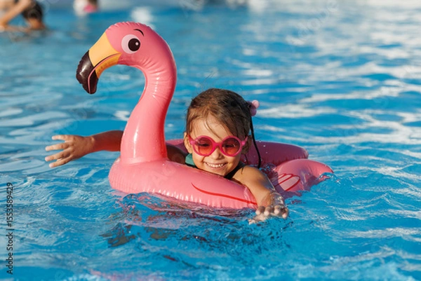 Fototapeta Cute funny toddler girl in a sunglasses relaxing on inflatable toy ring floating in pool have fun during summer vacation. Child having fun in swimming pool. 