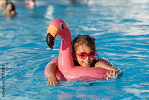 Fototapeta Cute funny toddler girl in a sunglasses relaxing on inflatable toy ring floating in pool have fun during summer vacation. Child having fun in swimming pool. 