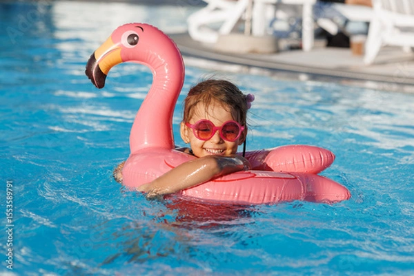 Fototapeta Cute funny toddler girl in a sunglasses relaxing on inflatable toy ring floating in pool have fun during summer vacation. Child having fun in swimming pool. 