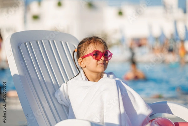 Fototapeta Funny little girl relaxing on summer vacation. The child has fun on the beach. Cute baby in a colorful swimsuit and sunglasses is resting.