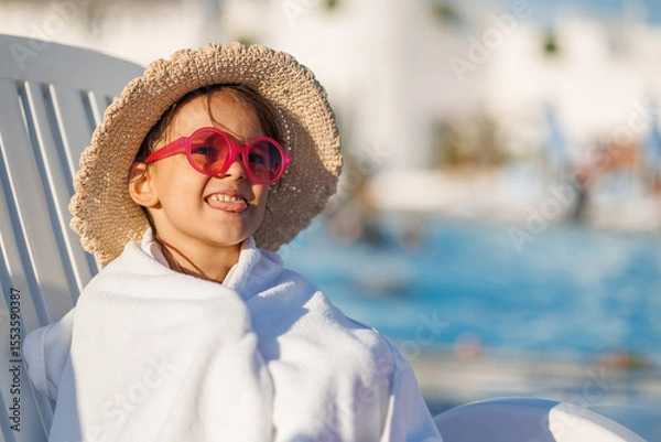 Fototapeta Funny little girl relaxing on summer vacation. The child has fun on the beach. Cute baby in a colorful swimsuit and sunglasses is resting.