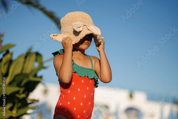 Fototapeta Funny little girl relaxing on summer vacation. The child has fun on the beach. Cute baby in a colorful swimsuit and sunglasses is resting.