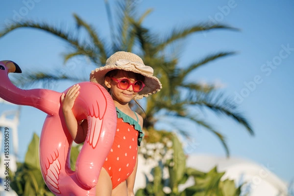 Fototapeta Funny little girl relaxing on summer vacation. The child has fun on the beach. Cute baby in a colorful swimsuit and sunglasses is resting.