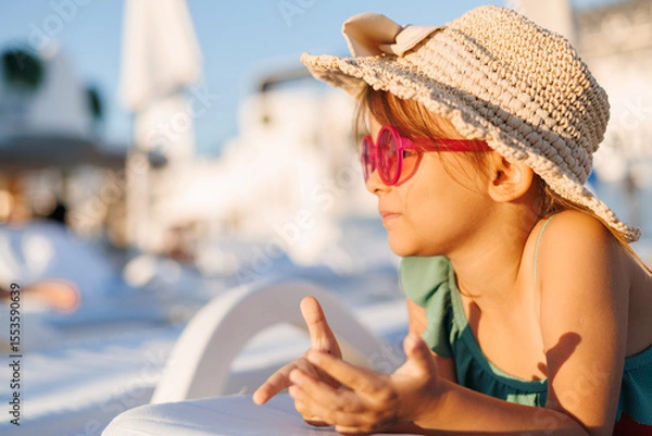 Fototapeta Funny little girl relaxing on summer vacation. The child has fun on the beach. Cute baby in a colorful swimsuit and sunglasses is resting.