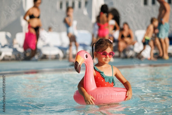 Fototapeta Cute funny toddler girl in a sunglasses relaxing on inflatable toy ring floating in pool have fun during summer vacation. Child having fun in swimming pool. 