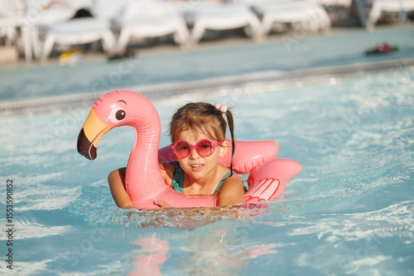 Fototapeta Cute funny toddler girl in a sunglasses relaxing on inflatable toy ring floating in pool have fun during summer vacation. Child having fun in swimming pool. 