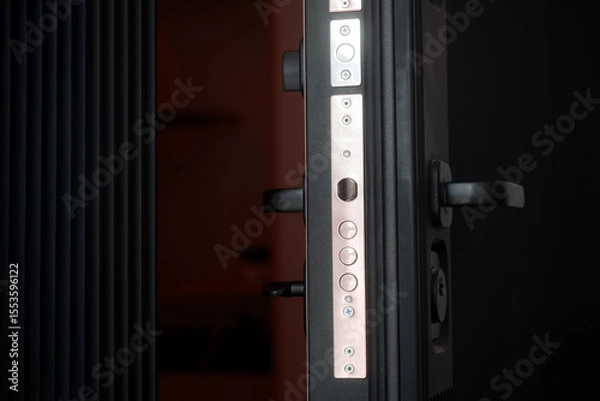 Obraz Partially opened black armored door revealing a metallic lock mechanism and dark interior hallway, evoking mystery and anticipation. Photo. Selective focusing