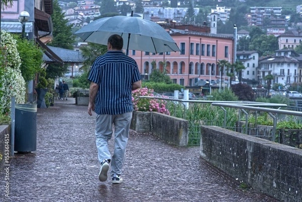 Fototapeta A man walks by the lake with an umbrella in the rain.