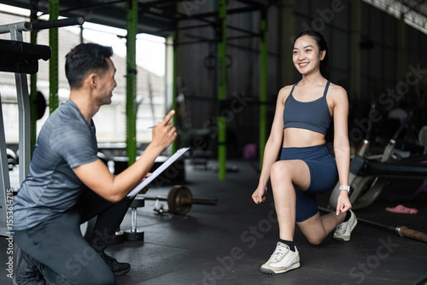 Obraz Fitness Coaching and Motivation. A trainer encouraging a woman during lunges in a gym setting.