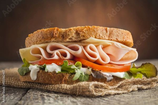 Obraz Tasty sandwich with ham, cheese, tomato and lettuce on wooden background