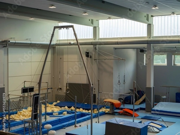 Obraz Modern gymnastics gym with training equipment: rings, pommel horse, parallel bars, mats, and foam pit. Indoor sports facility for physical education and acrobatics