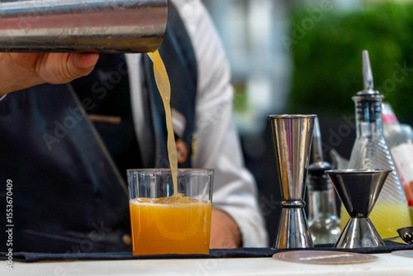 Fototapeta Bartender mixing orange cocktail with ice on a night club