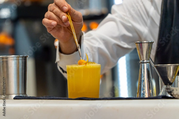 Fototapeta Bartender carefully placing orange slice on refreshing cocktail