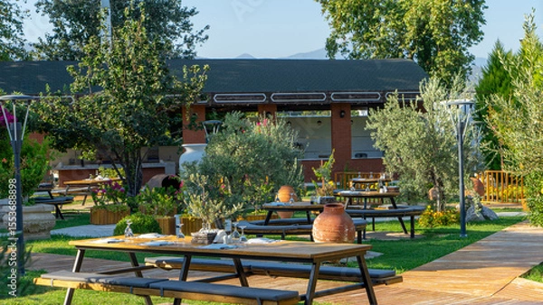 Fototapeta Wooden table in Mediterranean street restaurant with live olive tree on table. Tables set for lunch or dinner