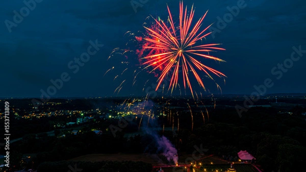 Fototapeta Colorful fireworks light up the night sky, creating a stunning display over a tranquil countryside landscape.