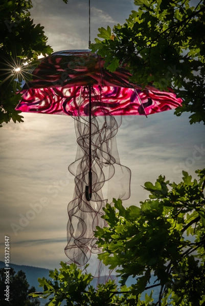 Fototapeta Umbrella suspended on green leaf tree with sunset color
