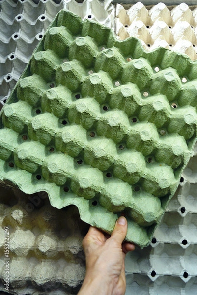 Fototapeta Zero waste and reuse concept: hand choosing cardboard egg carton from a stack, vertical photo. Paper pulp tray as symbol of recycling. Eco packaging material for storage and circular economy visuals