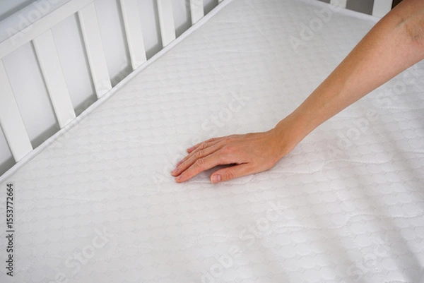 Obraz Young woman?s hands putting fitted sheet on baby crib mattress.